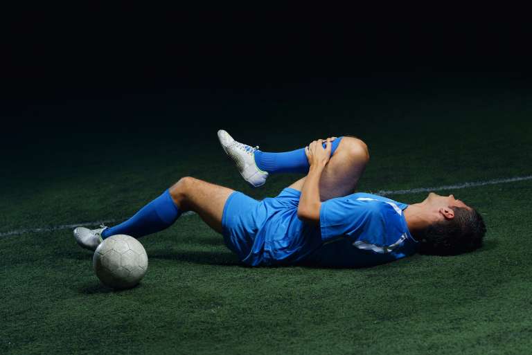 A photograph of a footballer, on the floor, holding their knee