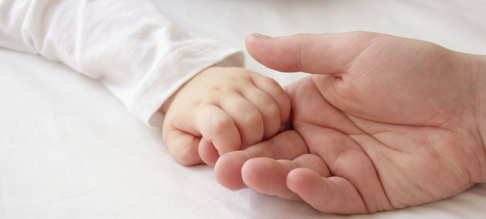 A photograph of a baby holding an adult's hand/finger. Pryers solicitors help people make birth injury claims.