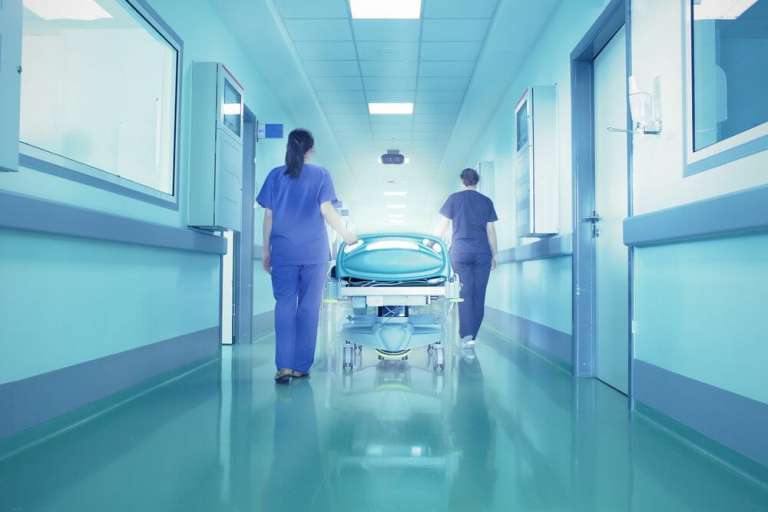 A photograph of a hospital bed being pushed down a ward, in an article about NHS treatment delays