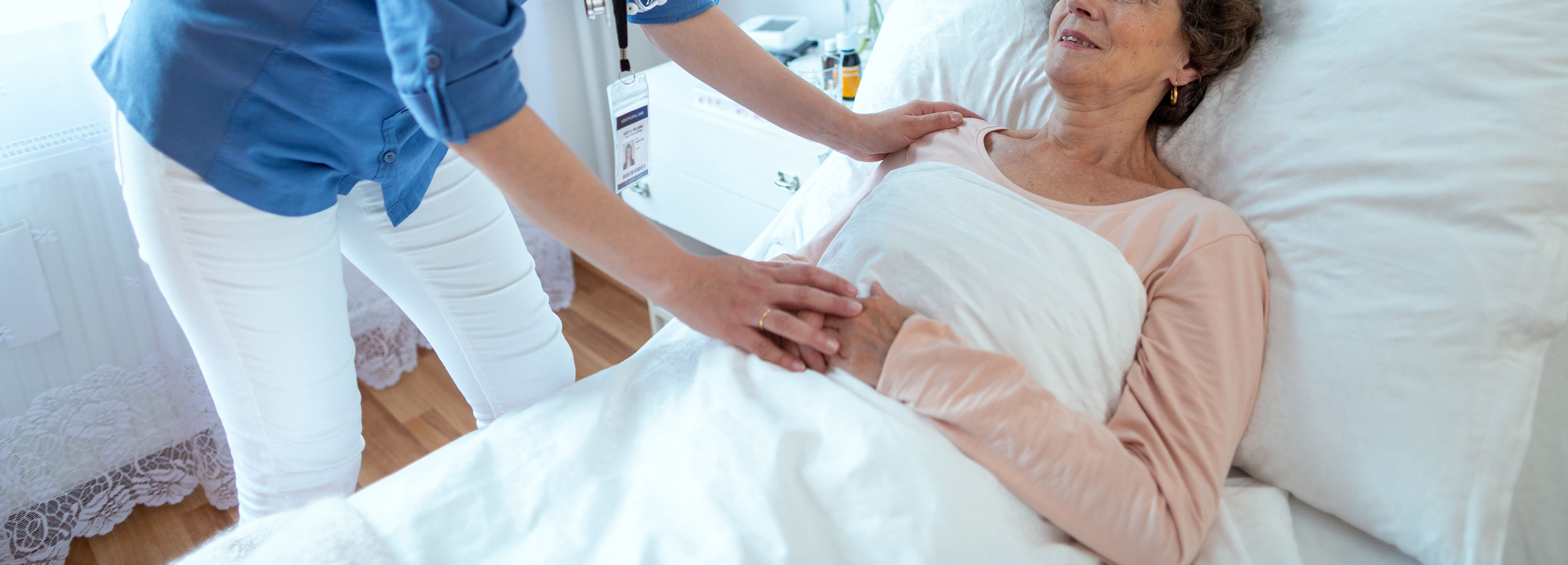 nurse leaning over elderly woman lying in hospital