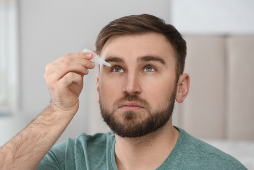 A photo of a man inserting eye drops into his eye