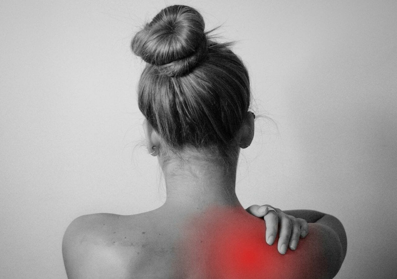 A photograph of a lady from behind, in black and white. The image has a red area added on her shoulder and she is grasping it, to depict pain, Mr Michael Walsh was an orthopaedic surgeon and operate on our client's shoulder