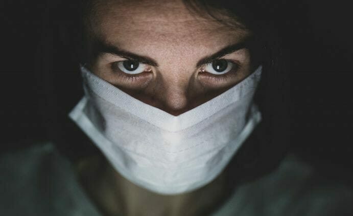 A photograph of a man in a mask, n a dark room. The image is to depict a rogue surgeon, in an article about the cost of rogue surgery to the NHS