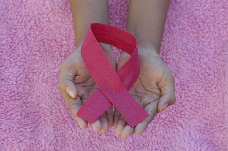 A pink ribbon, the symbol for breast cancer awareness, being held in two hands, against a pink background.