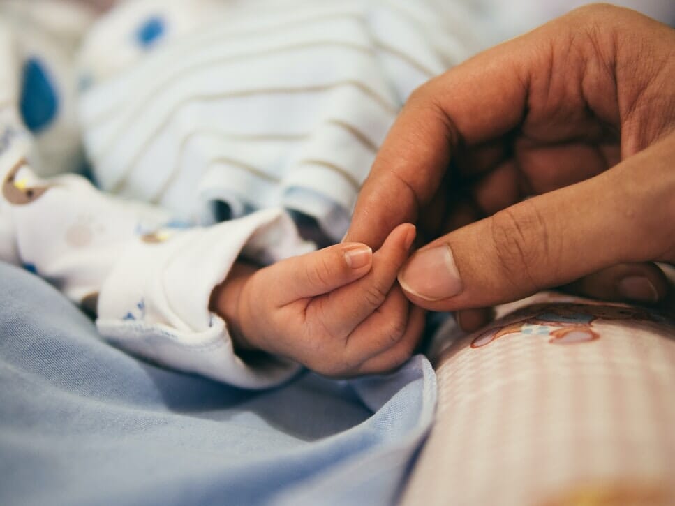 A photograph of a baby's hand being held by an adult, as the Patient Safety Minister announces £500,000 for maternity leadership training, to improve care for mothers and babies