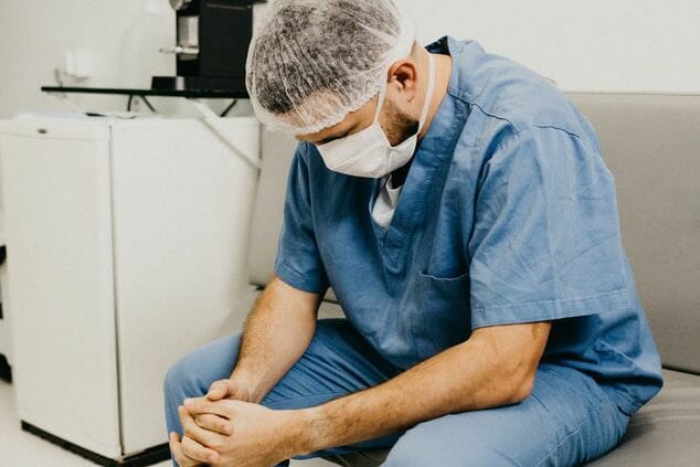 A photograph of a doctor in a face ask looking distressed.