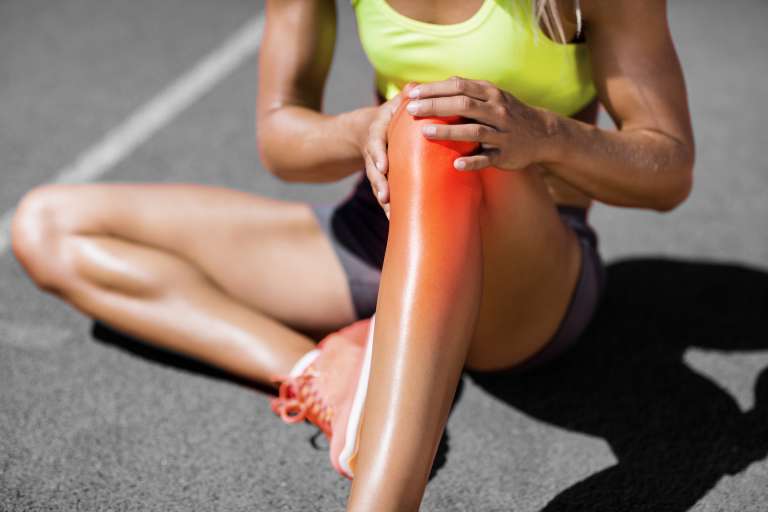 A photograph of a female athlete holding their knee, in pain,to depict the injury and problems following anterior cruciate ligament surgery that our client experienced