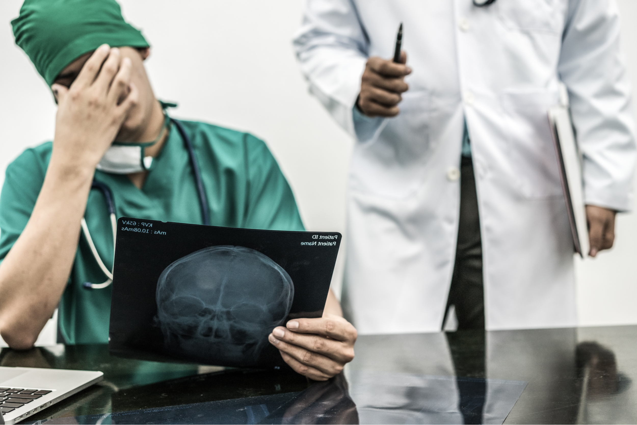 A photograph of a male doctor looking at a radiograph, with his head in his hand, to depict making a diagnostic error